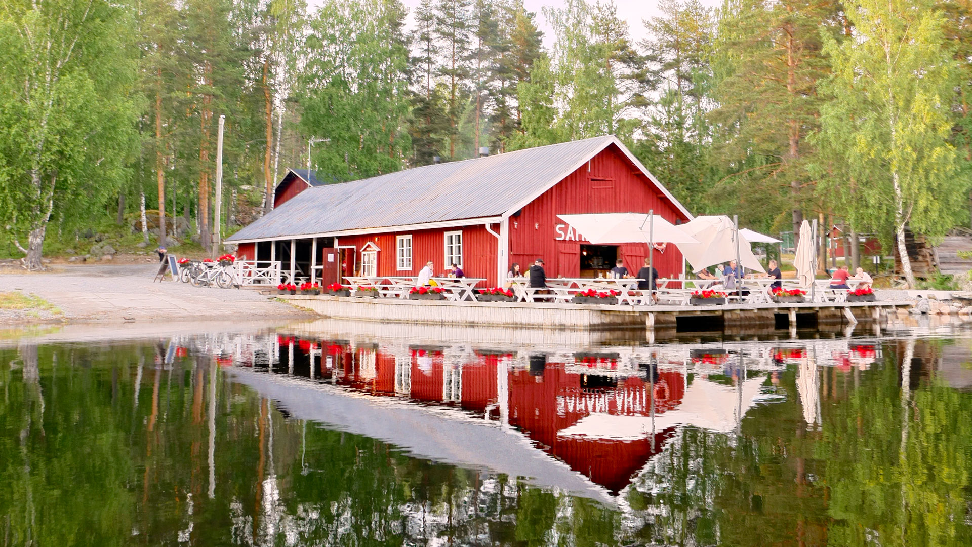 Pitkä puinen rakennus ja terassi aivan veden äärellä. 